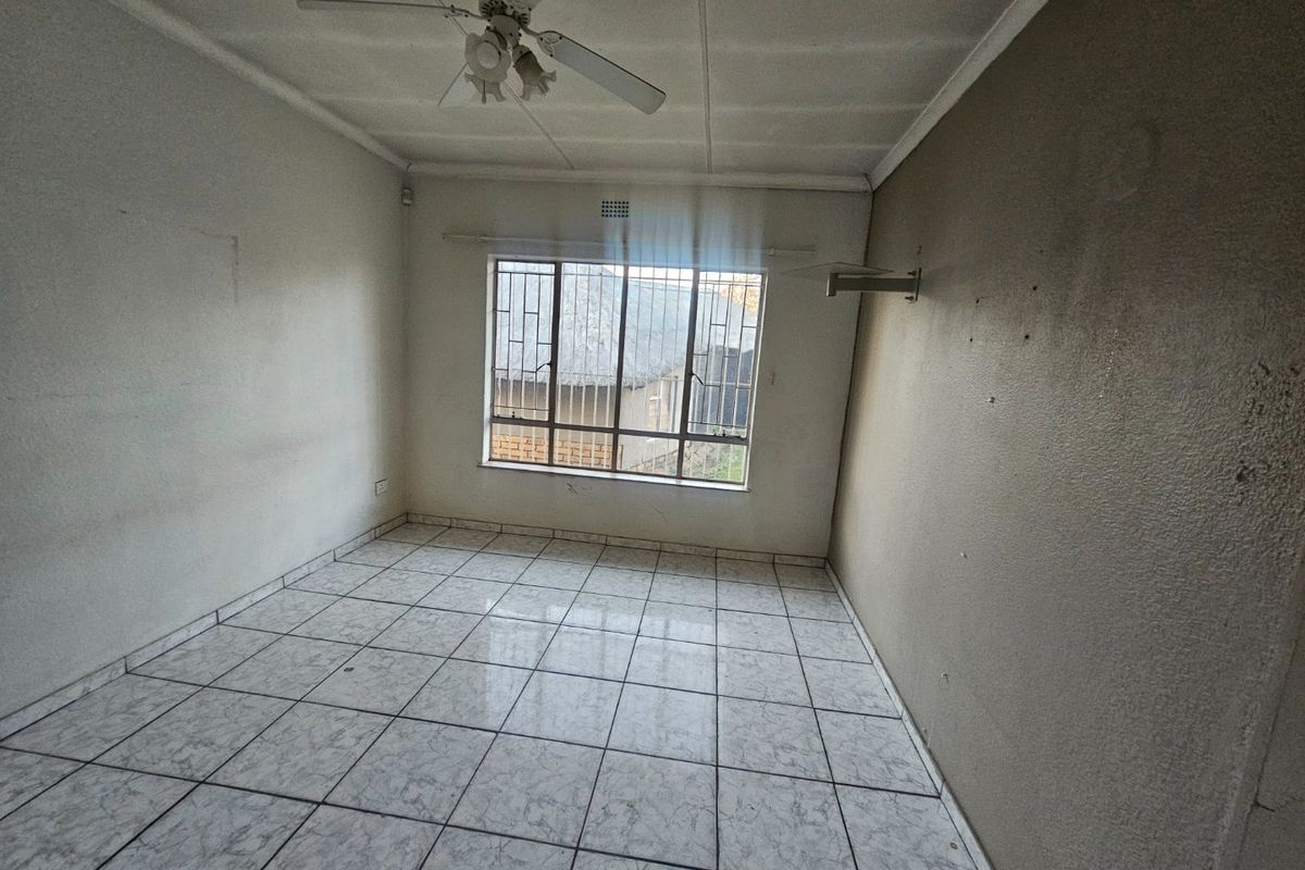 An empty bedroom featuring tiled flooring, a ceiling fan, and security bars on the window, requiring cosmetic updates to the wall surfaces.