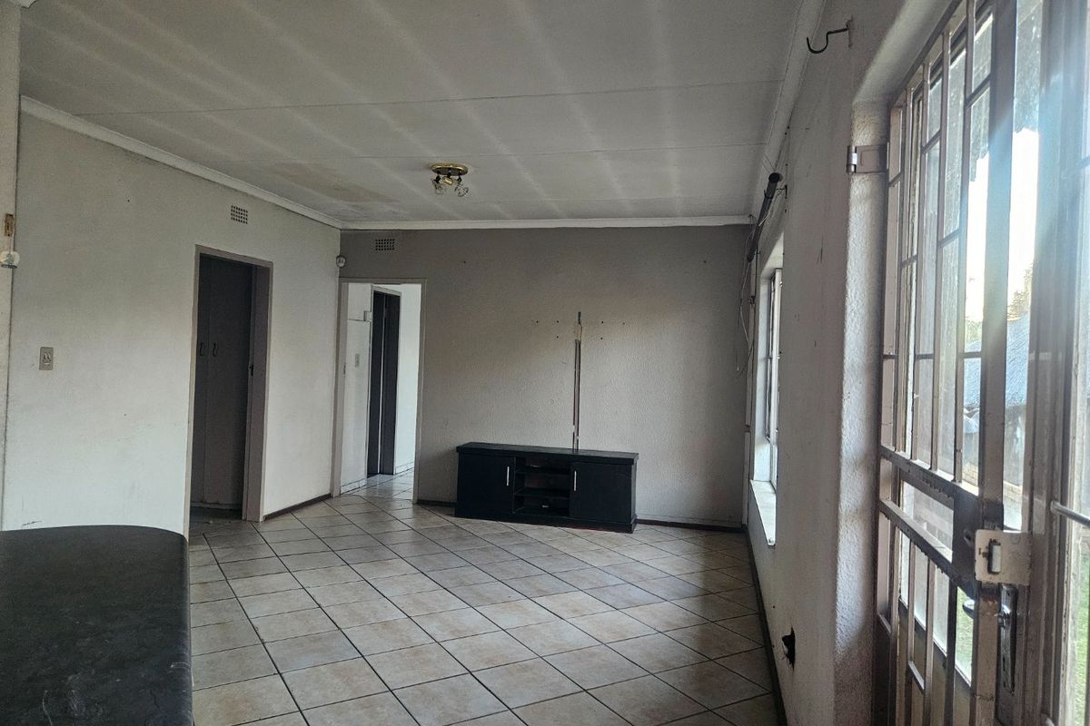 An empty living room featuring tiled flooring, a security gate, and neutral wall finishes, offering a blank canvas for renovation.