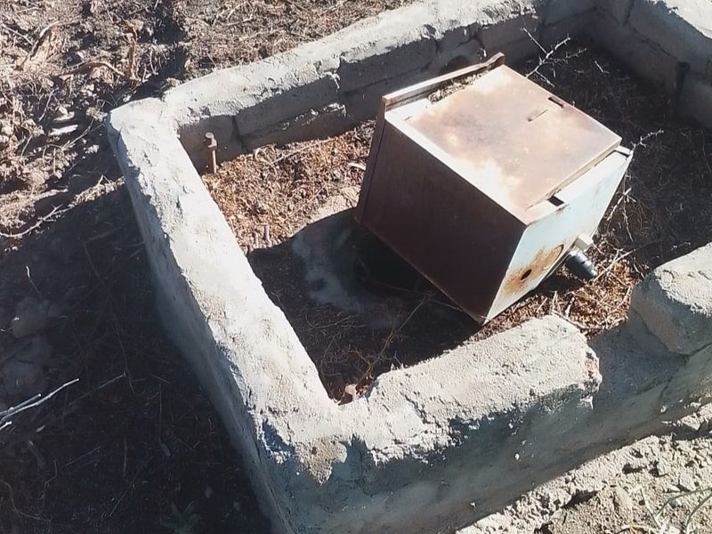 A view of a weathered concrete utility enclosure containing a corroded electrical box on the vacant residential land.