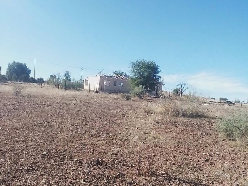 A view of a vacant residential plot featuring a dilapidated structure with a missing roof and perimeter fencing.