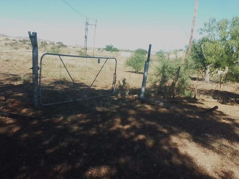A view of a vacant residential plot featuring a metal gate and wire mesh fencing with visible signs of wear.
