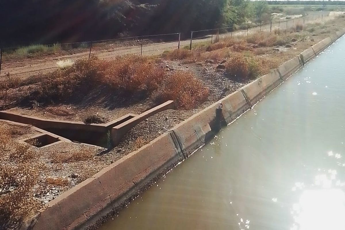 A view of a concrete irrigation canal and drainage infrastructure bordering a rural residential land parcel.