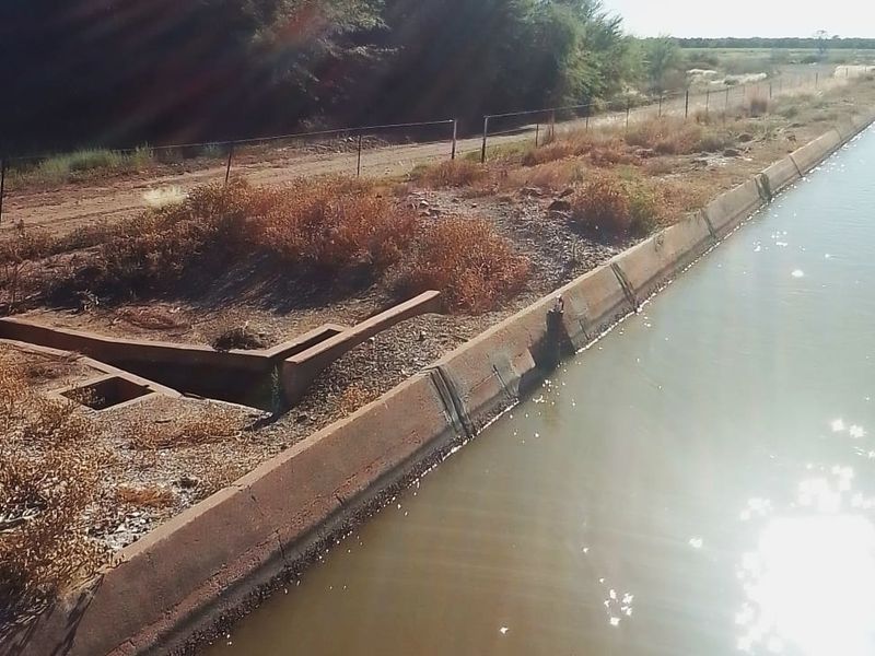 A view of a concrete irrigation canal and drainage infrastructure bordering a rural residential land parcel.