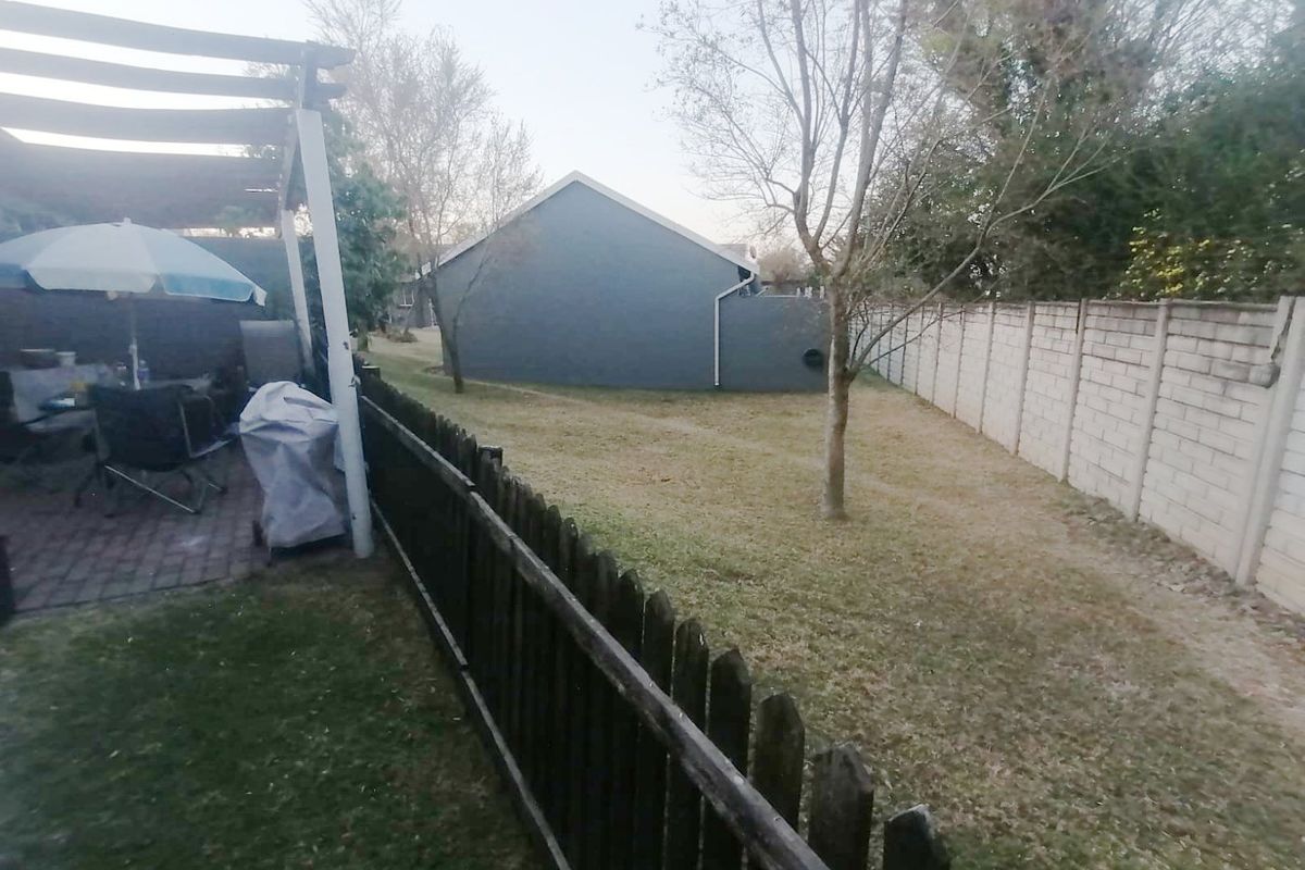 Rear garden area featuring a paved patio with a pergola, enclosed by a precast concrete boundary wall and a timber picket fence.
