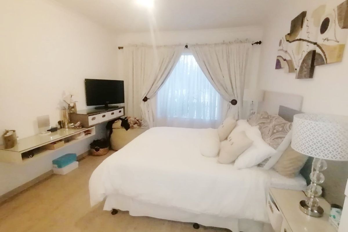 A neutrally decorated bedroom featuring a floating wall-mounted shelf and window treatments, offering a comfortable and functional living space.