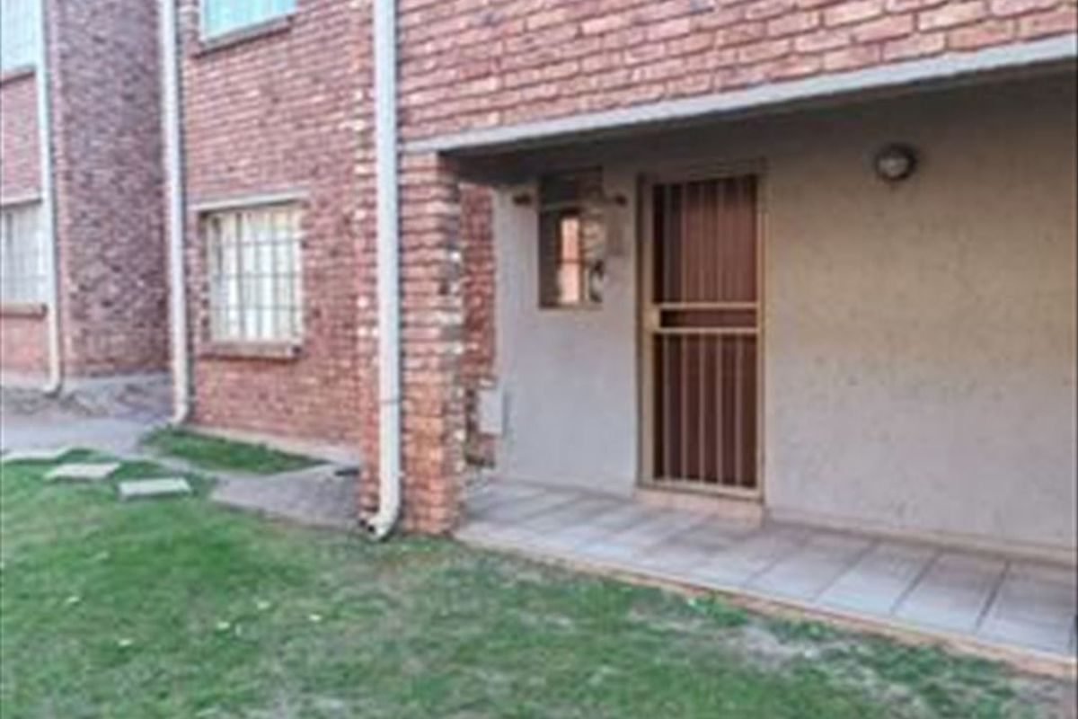 Rear view of the apartment building featuring a brick facade, a covered tiled patio area, and a secure entrance door.