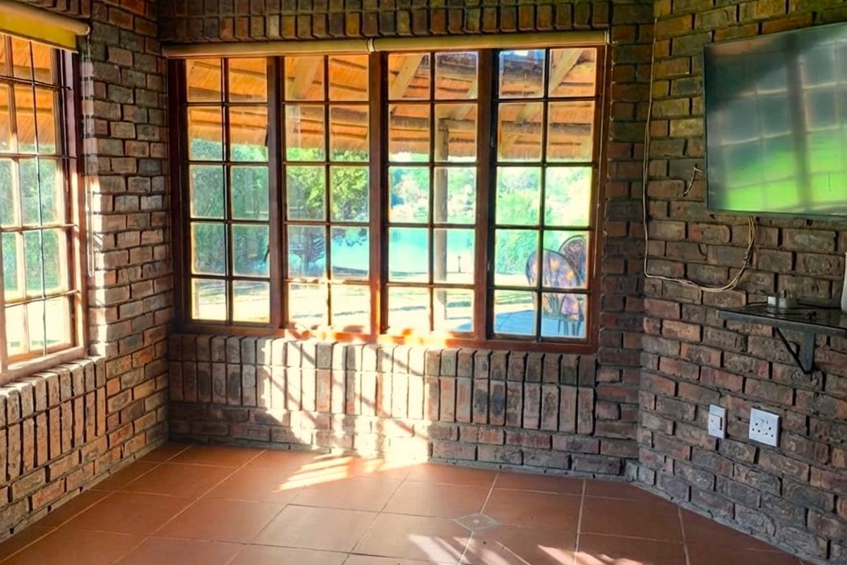 A rustic living area featuring exposed brick walls, terracotta floor tiles, and large timber-framed windows overlooking the garden.