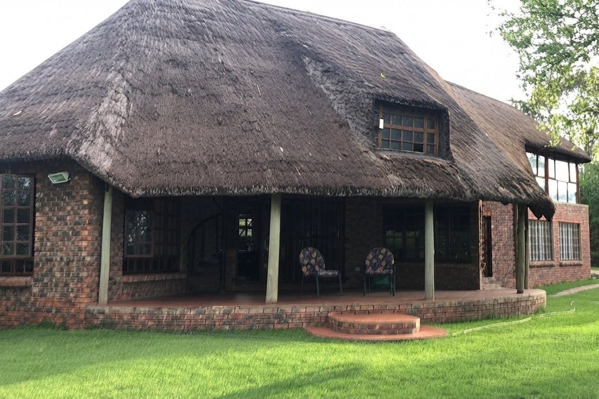 Rear view of a traditional thatch-roofed house featuring exposed brickwork, a covered patio area, and timber-framed windows overlooking a lawn.