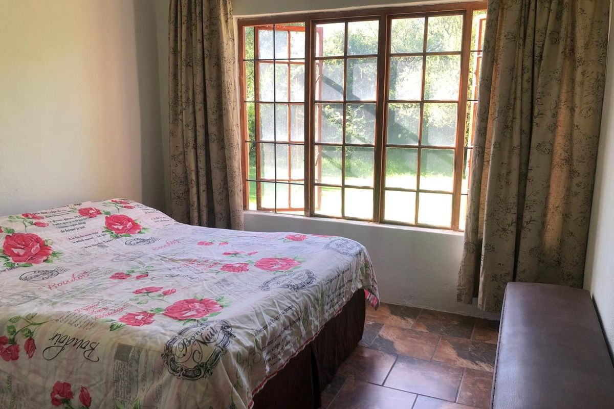 A bedroom featuring tiled flooring and large wooden-framed casement windows that provide natural light and garden views.