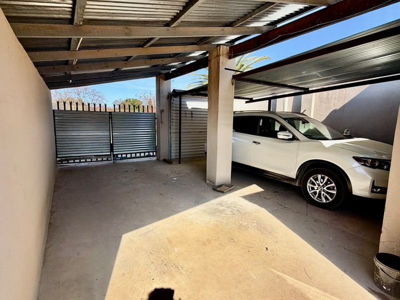 A covered carport or garage area featuring a corrugated metal roof, concrete flooring, and secure metal gate access.