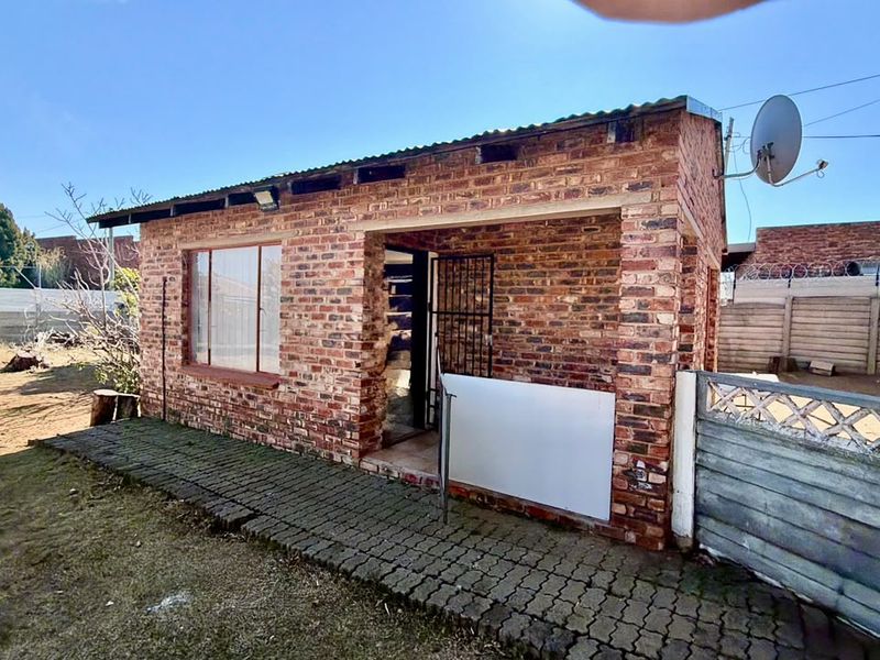 Rear view of a face brick house featuring a paved walkway, security gate, and precast concrete boundary walling.