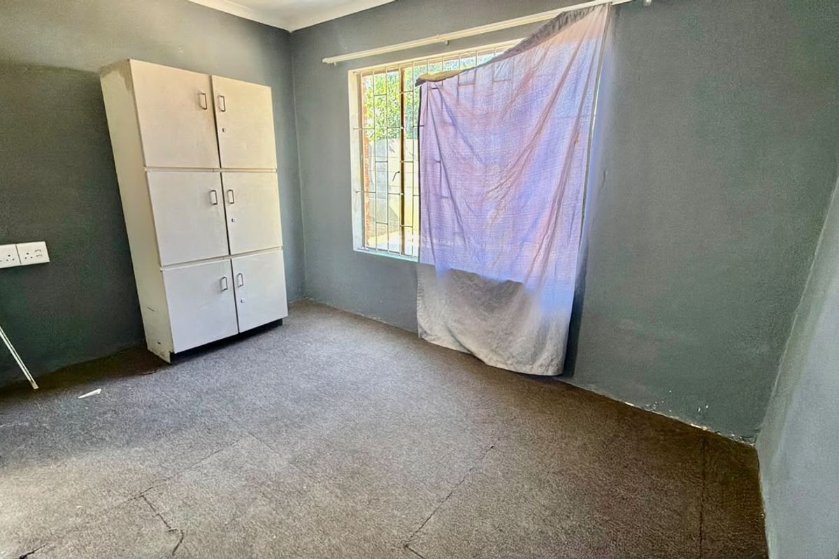 A vacant bedroom featuring built-in storage, security bars on the window, and carpeted flooring, offering a blank canvas for renovation.