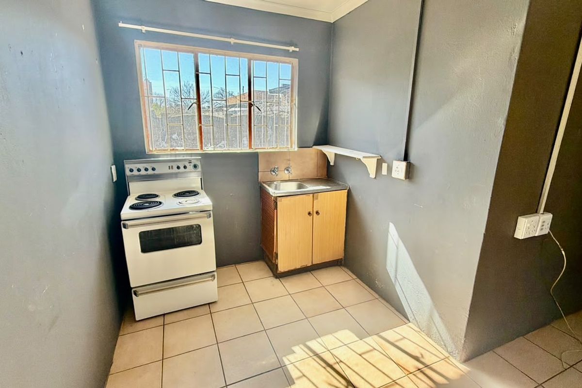A compact kitchen area featuring tiled flooring, a basic sink unit, and a freestanding stove, offering a functional space ready for modernization.