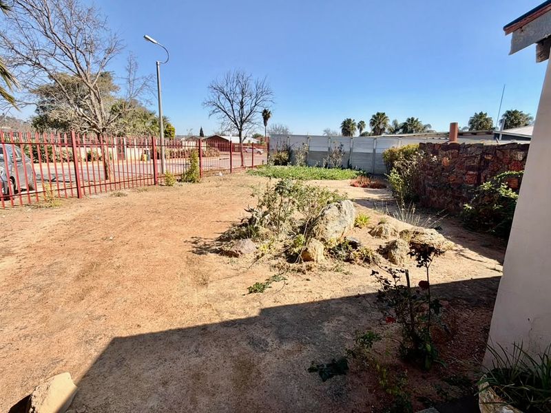 A spacious outdoor garden area featuring a rockery, perimeter metal fencing, and a stone boundary wall, offering potential for landscaping and outdoor improvement.