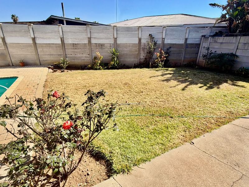 A backyard area featuring a swimming pool with paved surround, a concrete patio, and a precast concrete boundary wall.