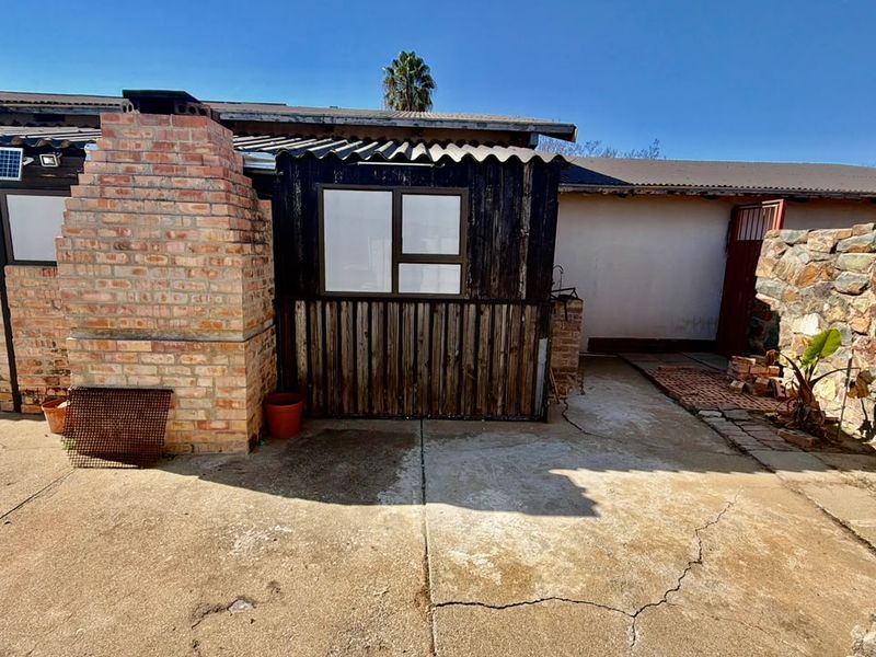 Rear exterior area featuring a brick fireplace, concrete patio, and stone retaining wall, showing signs of weathering and surface cracking.