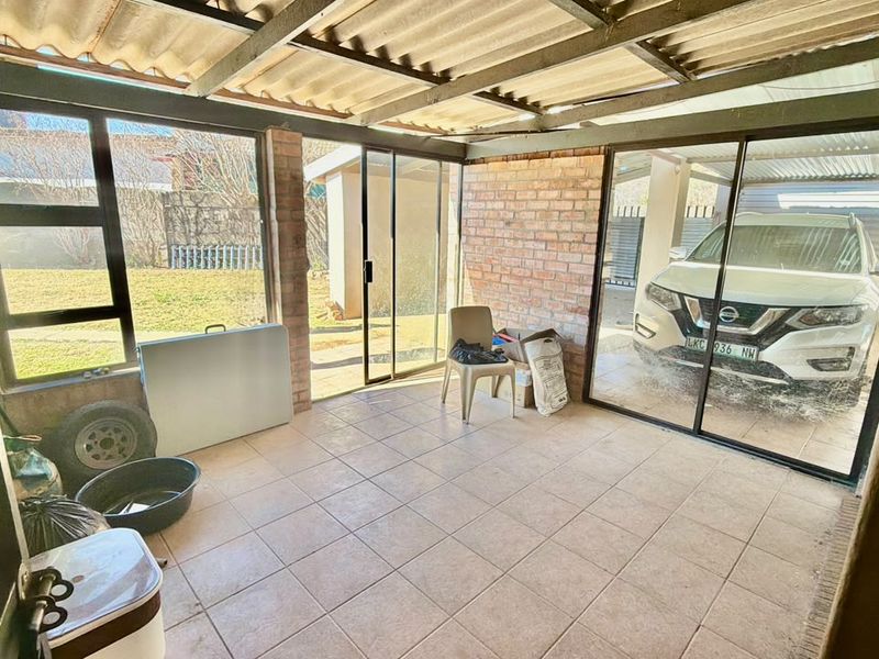 A covered patio area featuring tiled flooring, exposed brick walls, and sliding glass doors, offering a versatile outdoor space for relaxation or entertainment.