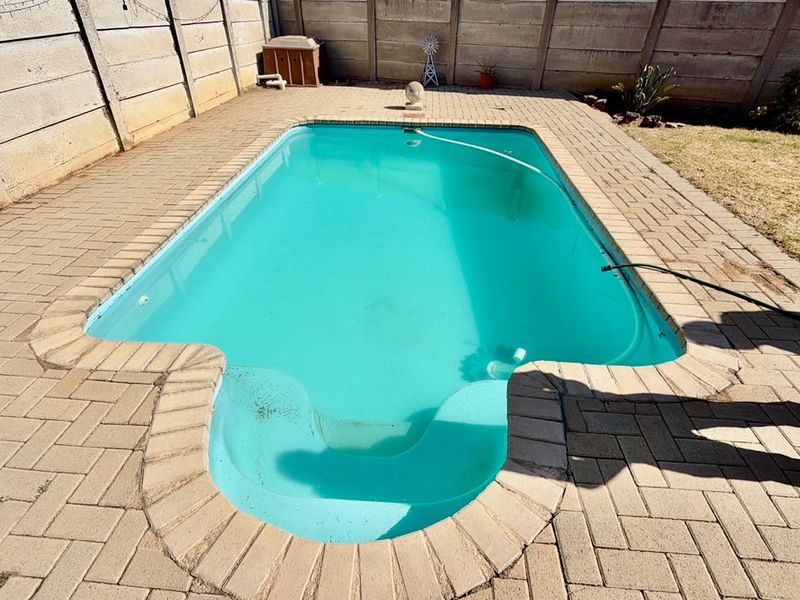 A rectangular swimming pool with a paved surround and precast concrete boundary wall in a private backyard setting.