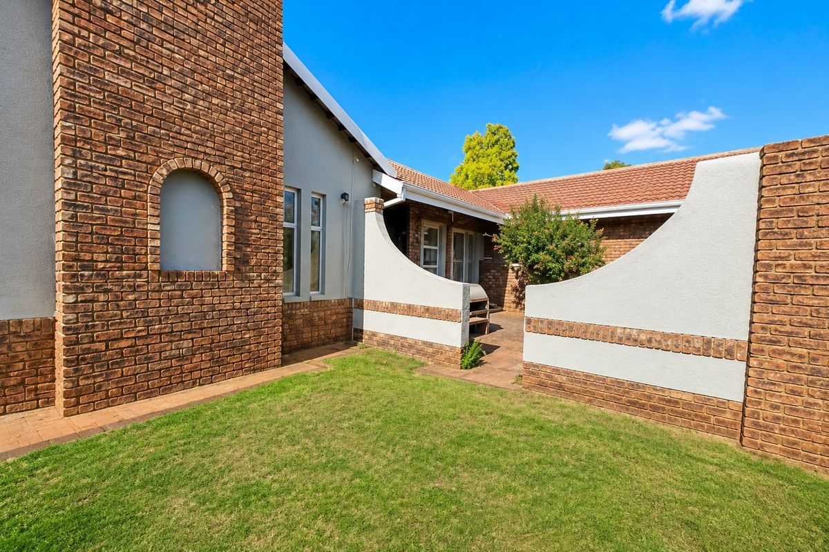A rear exterior view featuring a brick facade, a paved patio area with a built-in braai, and a small lawn.