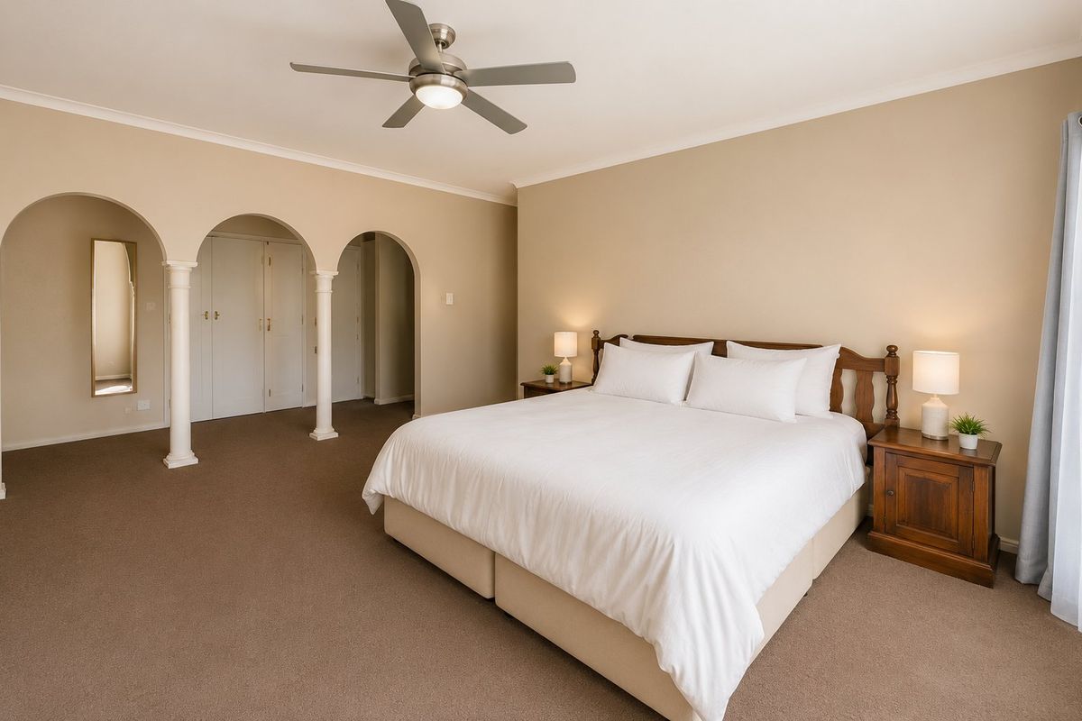 Spacious bedroom featuring neutral carpeting, a ceiling fan, and distinctive arched architectural details leading to a built-in wardrobe area.