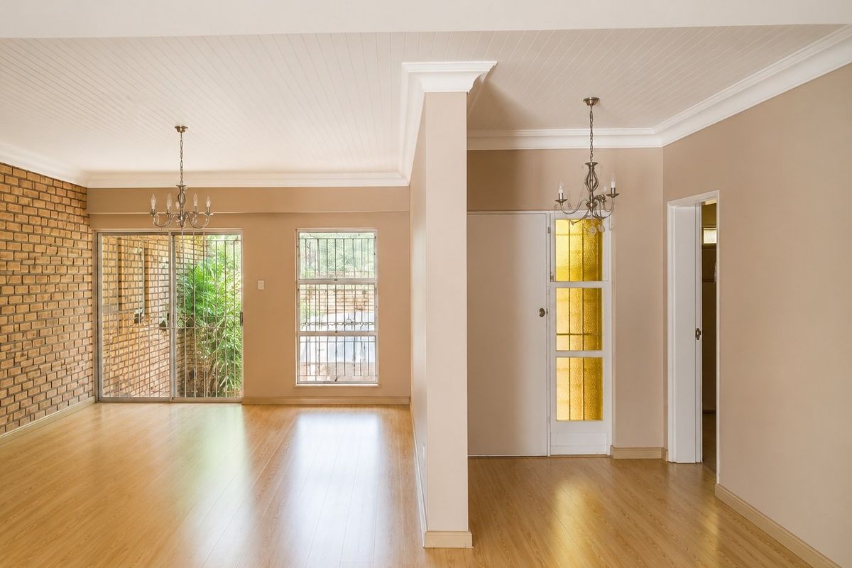 Spacious living area featuring laminate flooring, an exposed brick feature wall, beadboard ceiling with crown molding, and access to an outdoor area.