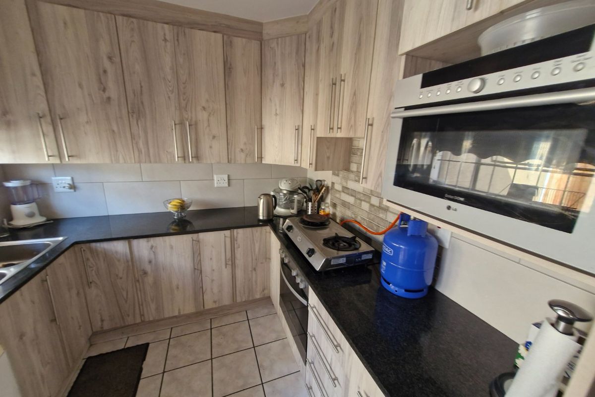 A functional kitchen featuring light wood-grain cabinetry, dark granite countertops, built-in oven, gas hob, and integrated microwave with tiled flooring and backsplash.
