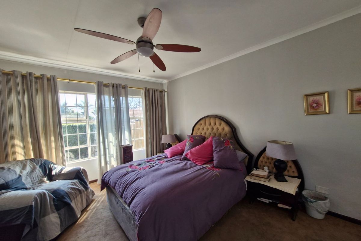 A spacious bedroom featuring a ceiling fan, carpeted flooring, and large windows with curtain rails, offering a comfortable and functional living space.