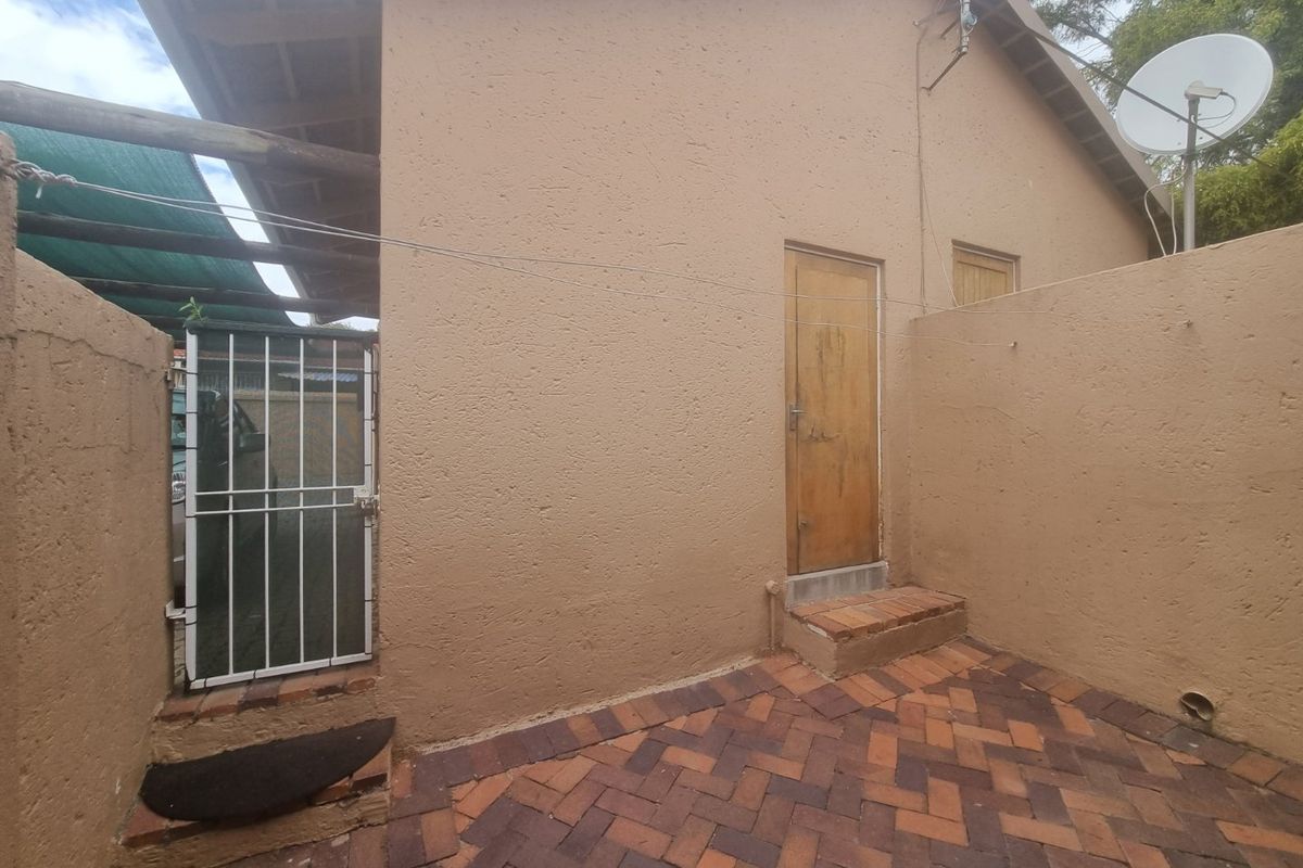 Rear exterior view of the townhouse featuring a paved courtyard, boundary wall, and access door with a security gate.