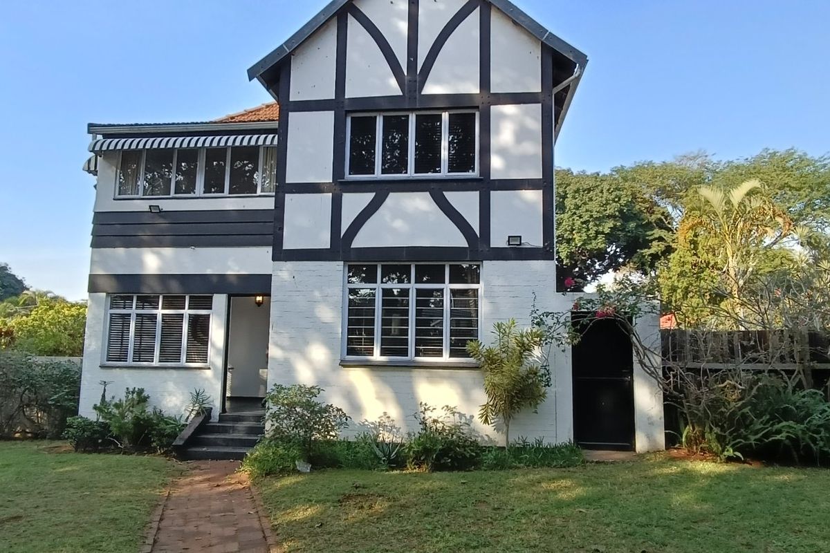 Rear view of a two-story Tudor-style house featuring a distinctive timber-framed facade, casement windows with security bars, and a landscaped garden.
