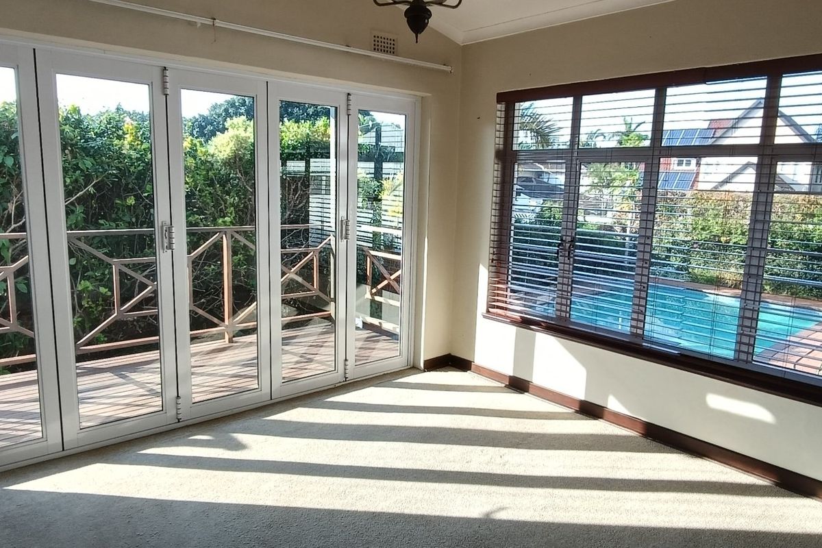 Bright and spacious living area featuring large windows and bi-fold doors opening onto an outdoor deck with pool views.