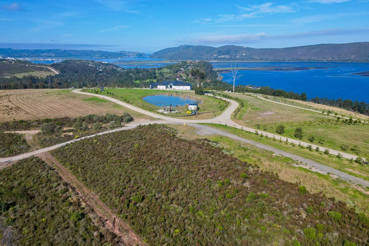 Aerial view of a large, undeveloped residential land parcel featuring gravel access roads, a small pond, and expansive coastal landscape views.