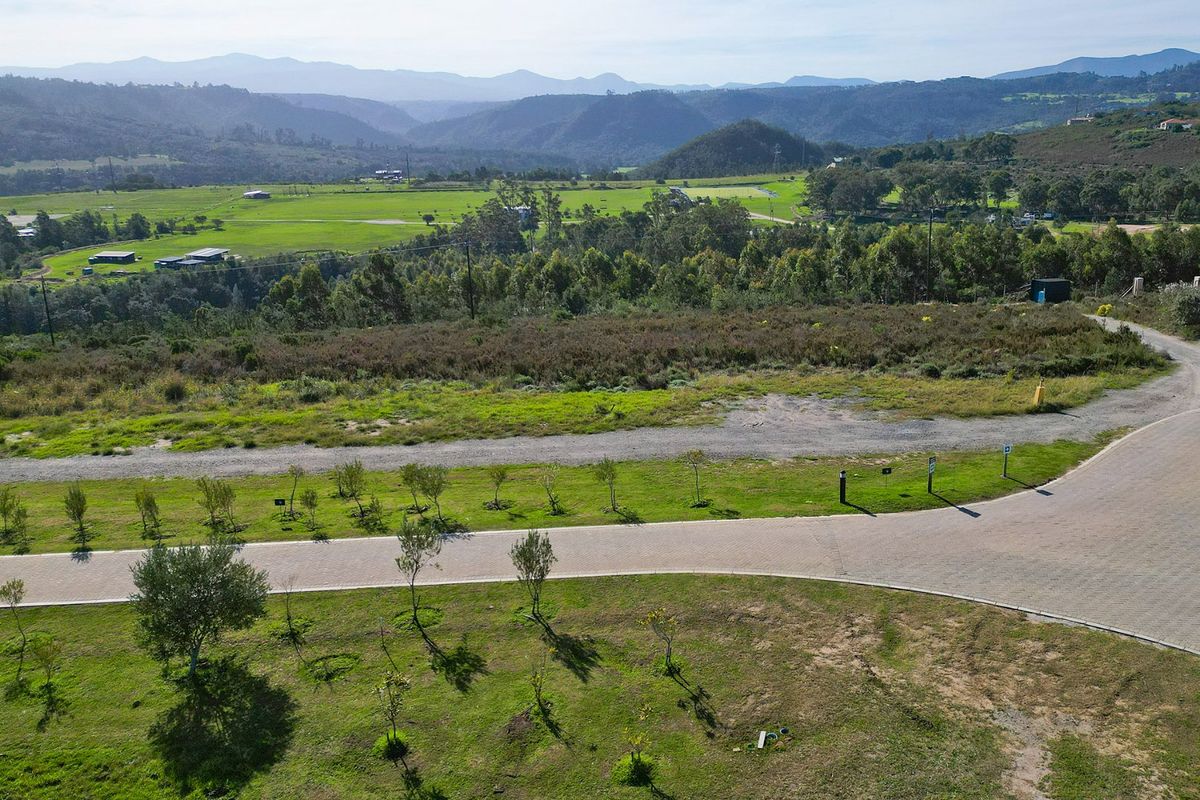 An aerial view of a vacant residential plot featuring paved road access and expansive views of the surrounding green landscape and mountains.
