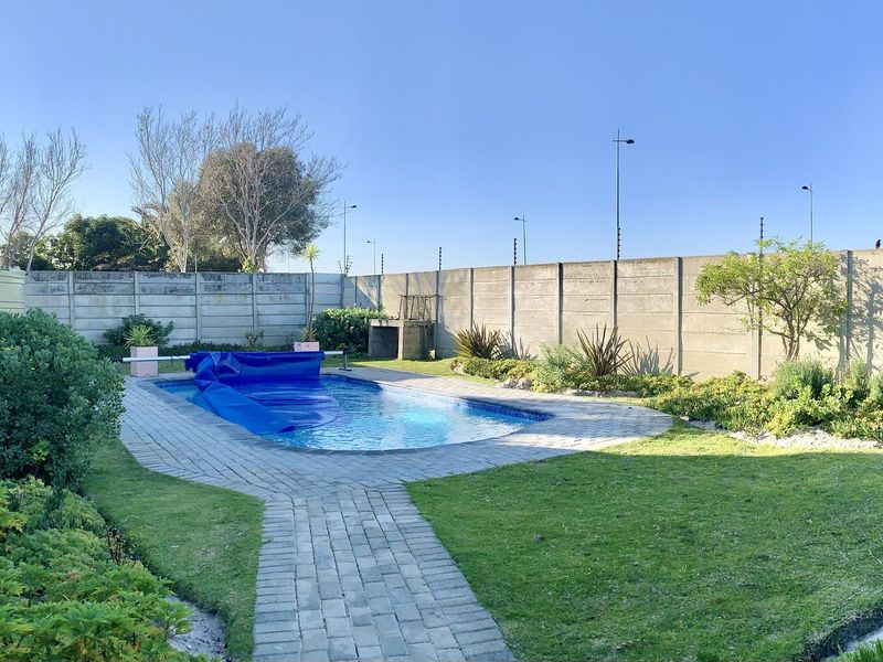 Private backyard featuring a swimming pool with a cover, paved pathways, a built-in braai, and a secure precast concrete boundary wall.