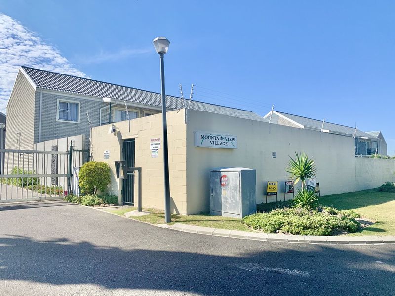 Front entrance view of Mountain View Village apartment complex featuring a secure gated access point, boundary wall, and electric fencing.