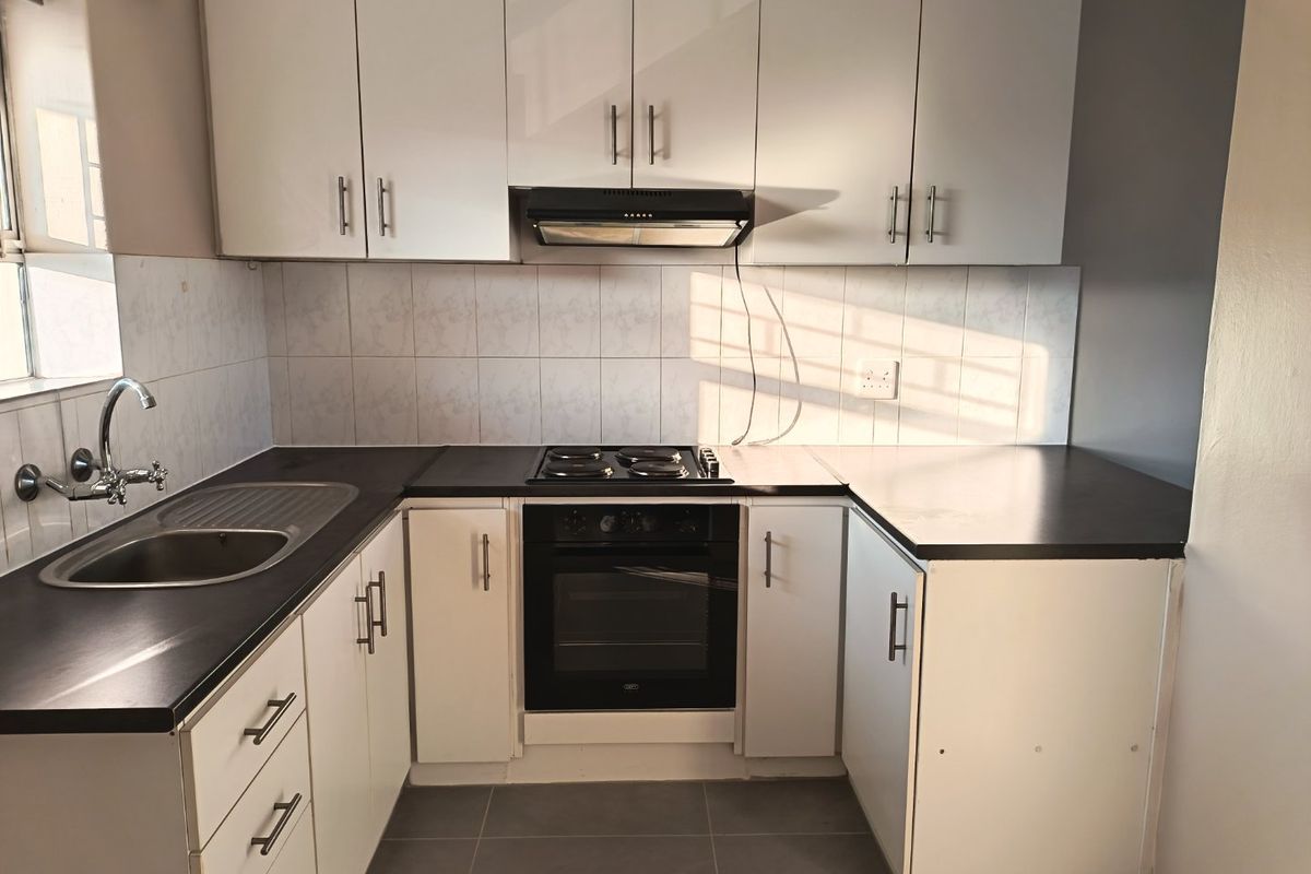 A functional kitchen featuring white cabinetry, dark laminate countertops, built-in oven and hob, tiled backsplash, and tiled flooring.