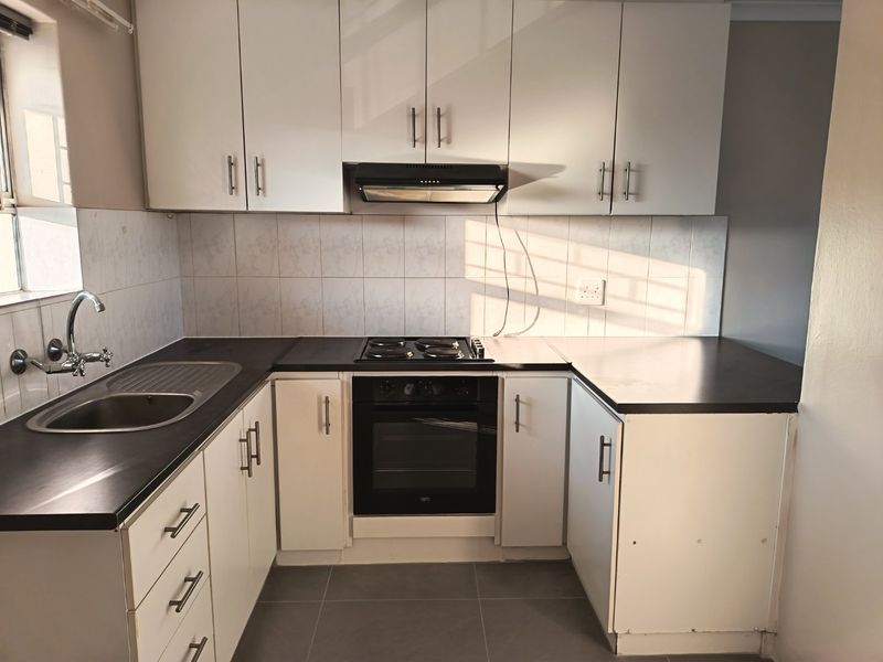 A functional kitchen featuring white cabinetry, dark laminate countertops, built-in oven and hob, tiled backsplash, and tiled flooring.