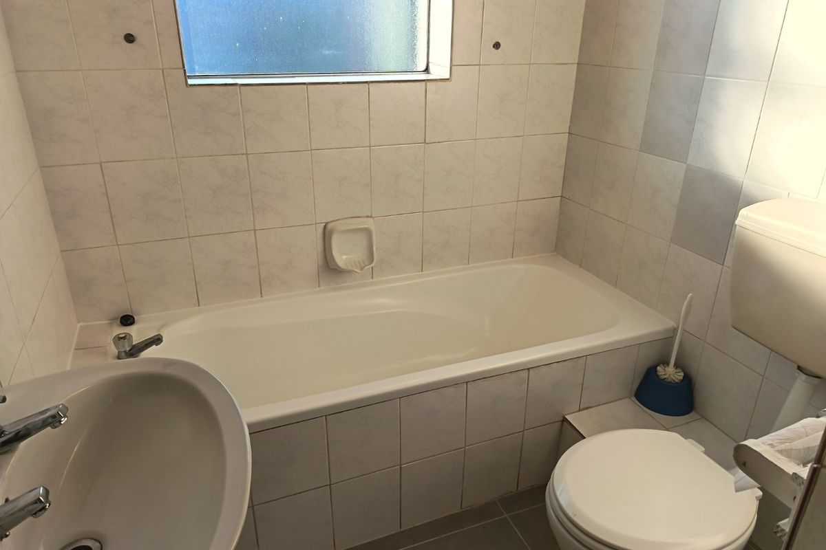 A functional bathroom featuring a standard bathtub, pedestal basin, and toilet with neutral wall and floor tiling.