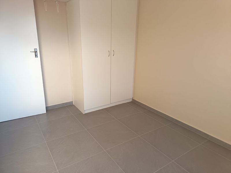 A clean, empty bedroom featuring neutral tiled flooring and a built-in white wardrobe, offering a blank canvas for personalization.
