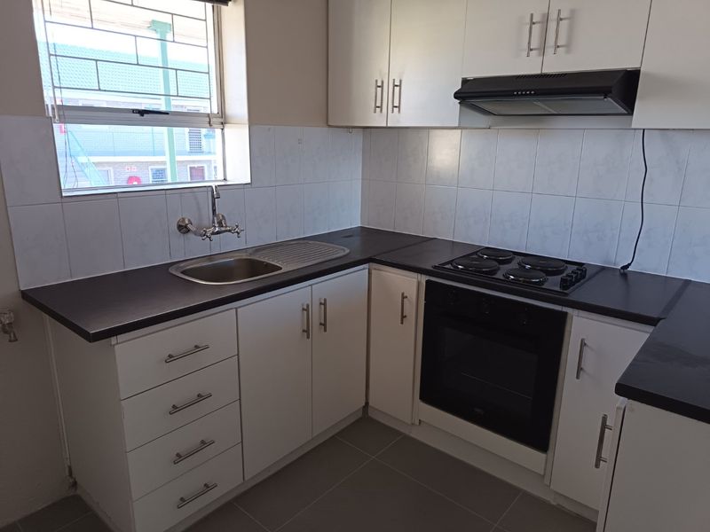 A clean and functional kitchen featuring white cabinetry, dark laminate countertops, built-in oven, electric hob, and a tiled backsplash with a window view.