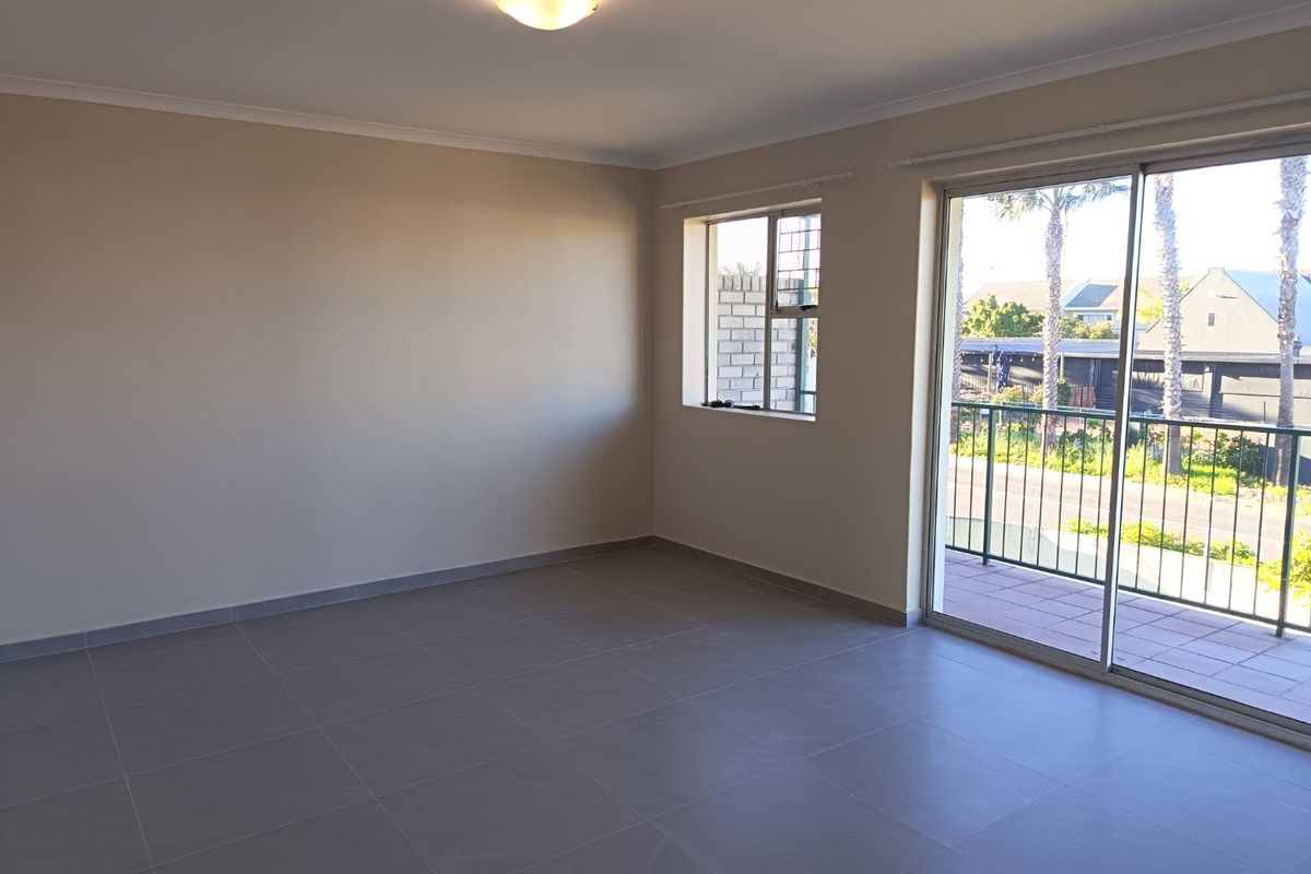 A bright, empty living room featuring neutral tiled flooring and a large sliding glass door providing access to a private balcony.