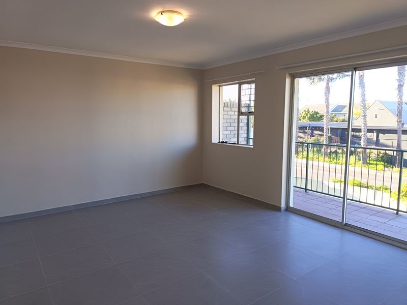 A bright, empty living room featuring neutral tiled flooring and a large sliding glass door providing access to a private balcony.