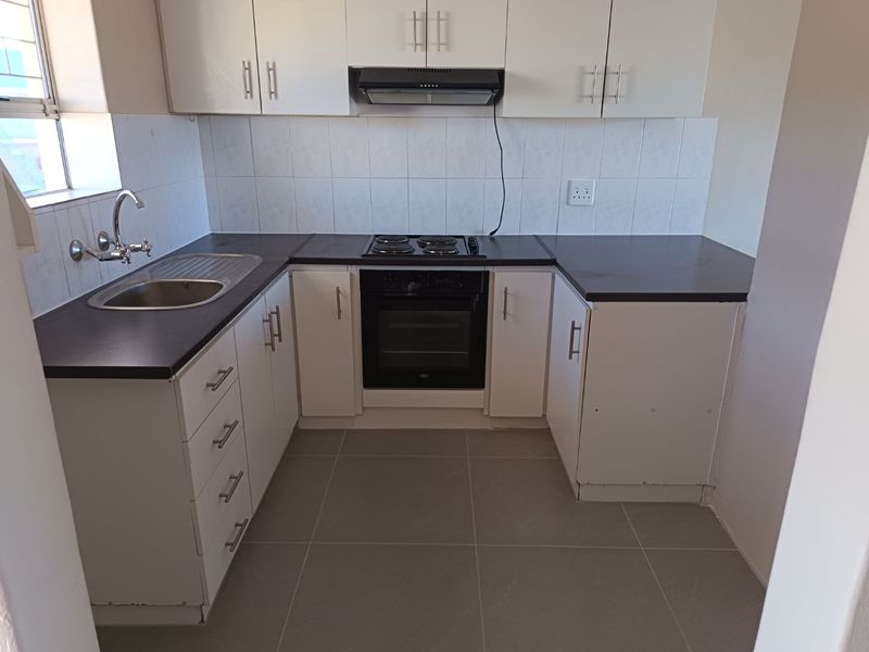 A functional, compact kitchen featuring white cabinetry, dark countertops, tiled splashbacks, and integrated appliances including an oven, hob, and extractor fan.