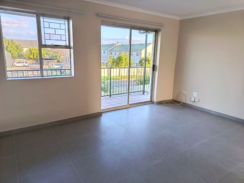 An empty, well-lit living room featuring modern grey floor tiles, a sliding glass door leading to a balcony, and neutral wall finishes.