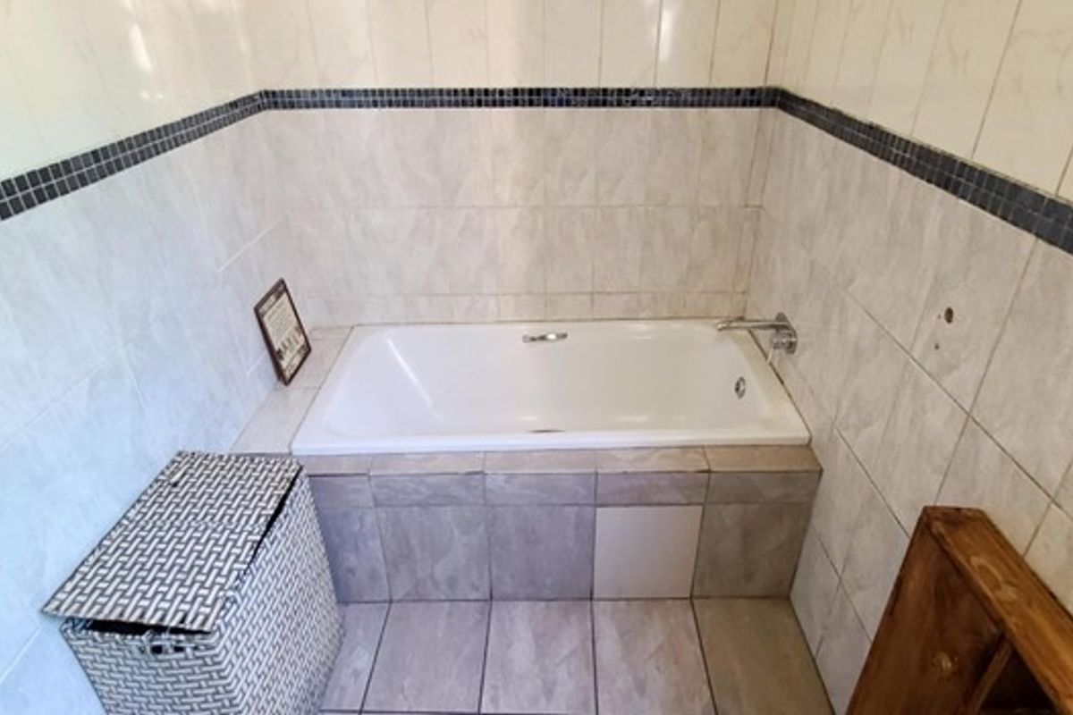 A bathroom featuring a built-in bathtub with tiled surround and wall tiling, currently showing signs of wear and missing finishes.