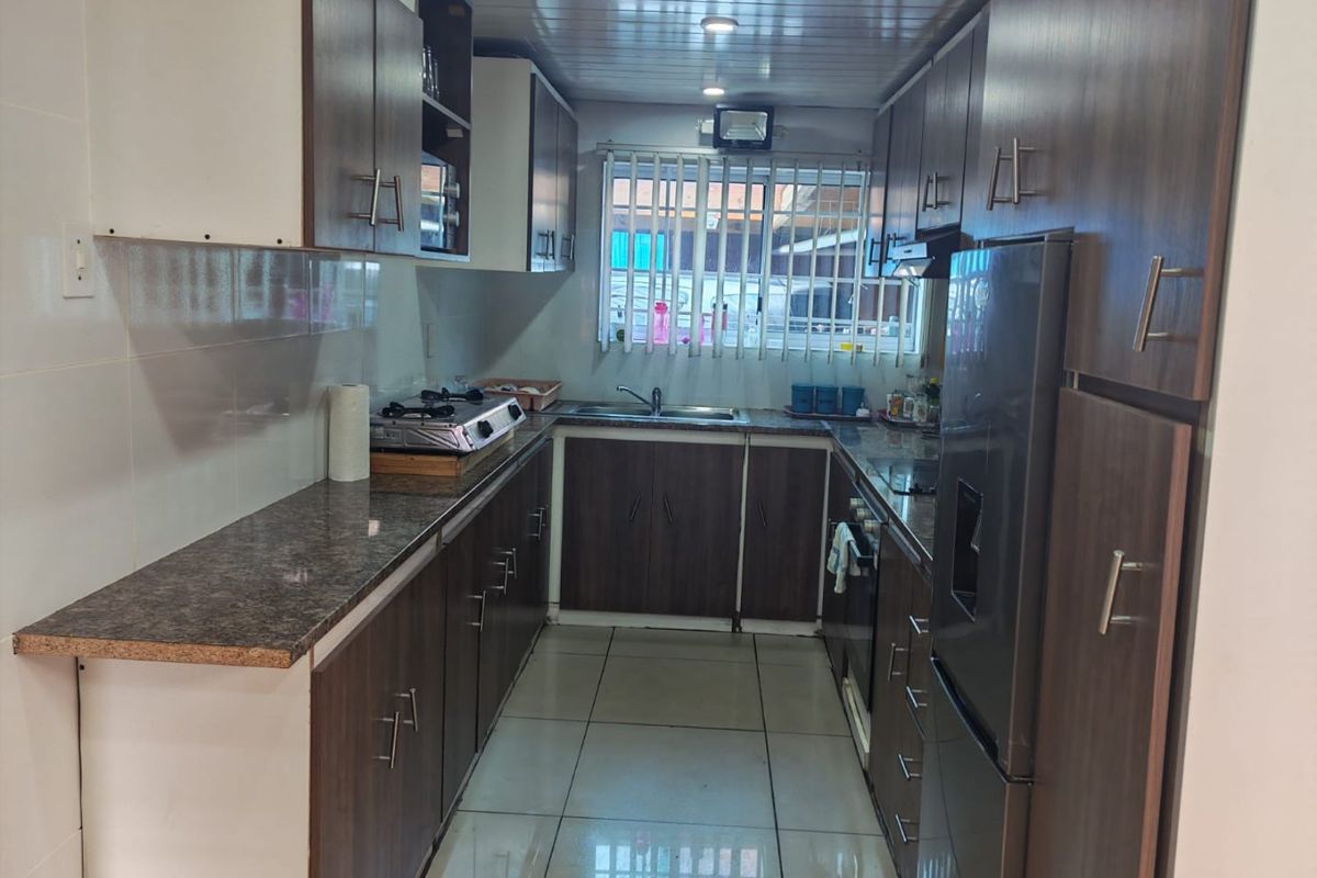 A functional galley-style kitchen featuring dark wood-look cabinetry, granite-effect countertops, tiled flooring, and integrated appliances.