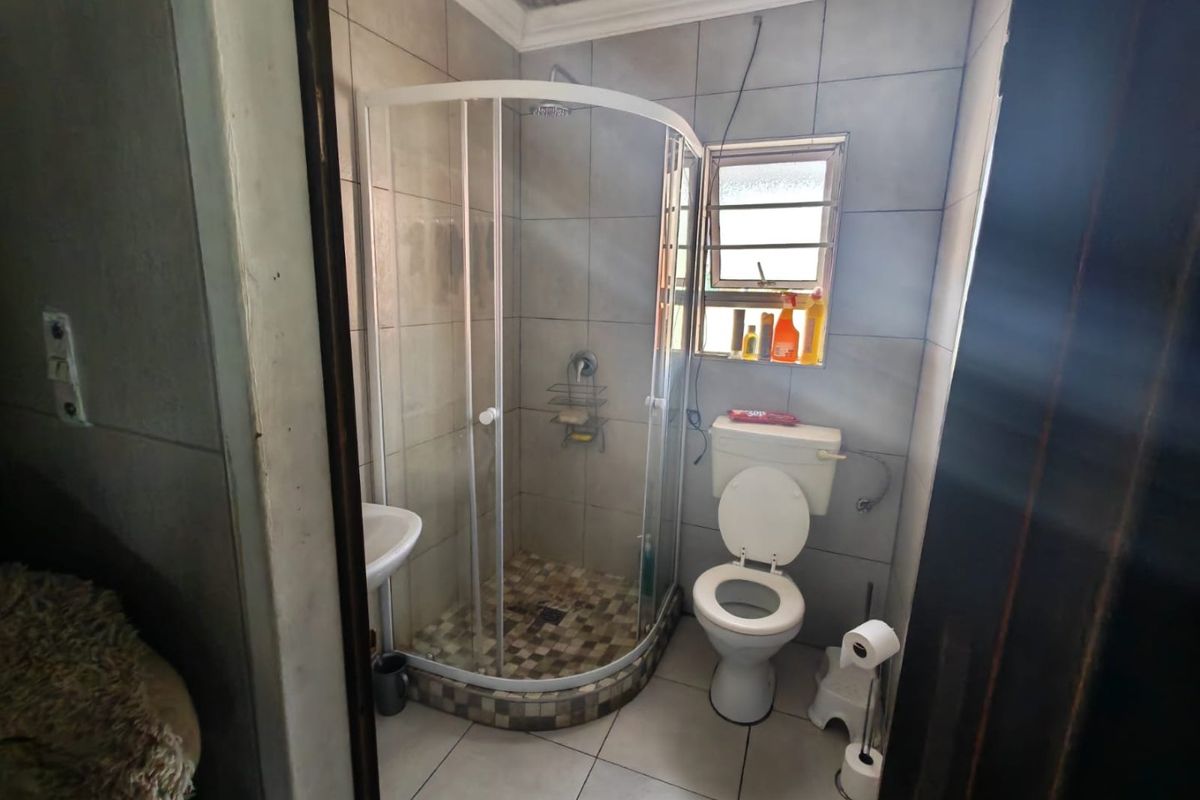 Compact bathroom featuring a corner shower enclosure, tiled walls and floors, a standard toilet, and a washbasin.