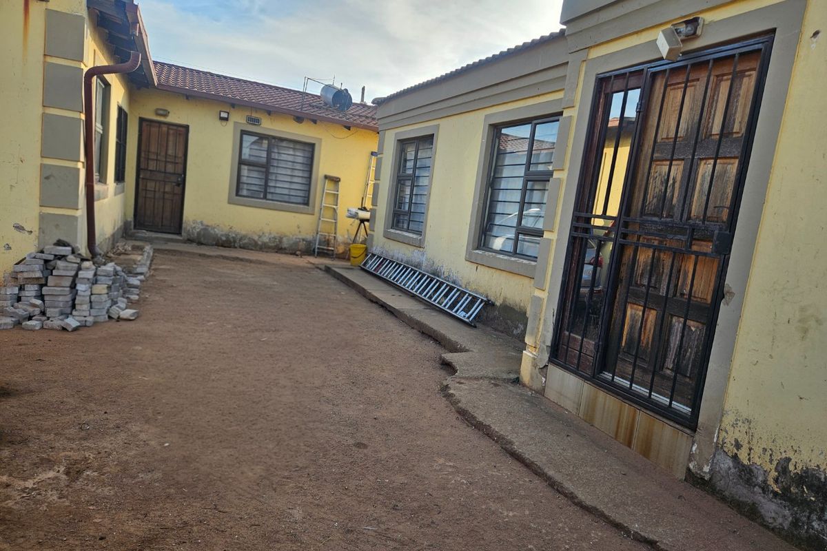 Rear exterior view of the property showing a courtyard area with concrete apron, security gates, and weathered exterior wall finishes.