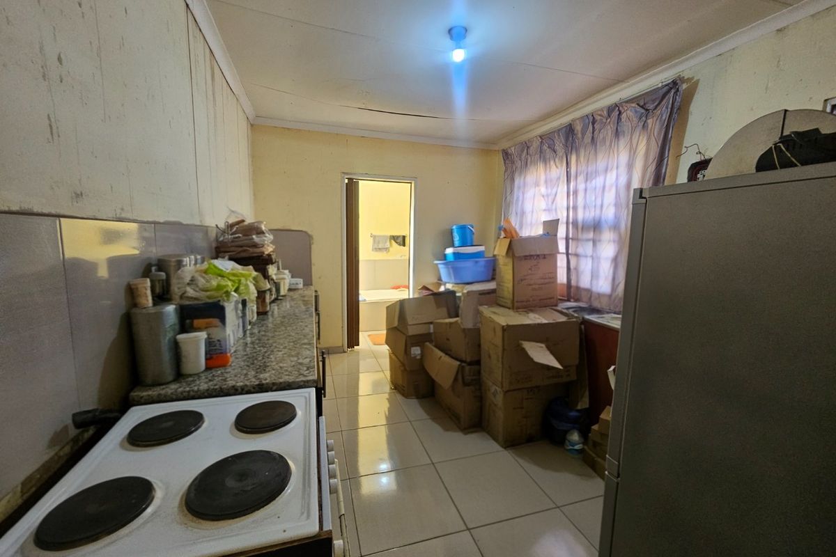 A dated kitchen featuring tiled flooring, granite countertops, and an electric hob, currently in need of significant cosmetic renovation and repair.