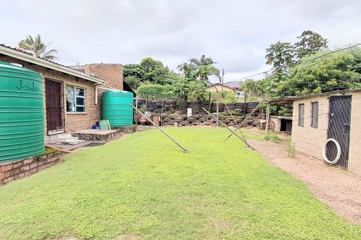 Rear garden area featuring a lawn, brick outbuilding, and large water storage tanks against the main house structure.