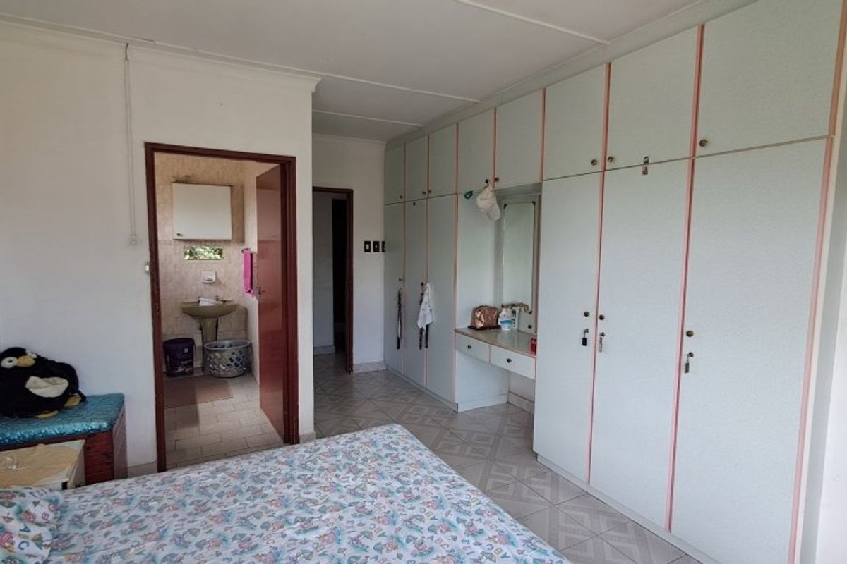 Bedroom featuring extensive built-in cupboards with integrated vanity and an adjoining en-suite bathroom, showcasing dated finishes throughout.